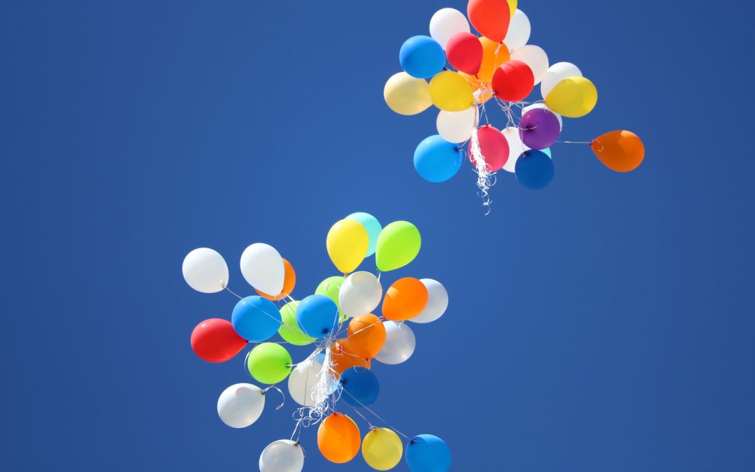 bunches of birthday balloons floating across a blue sky